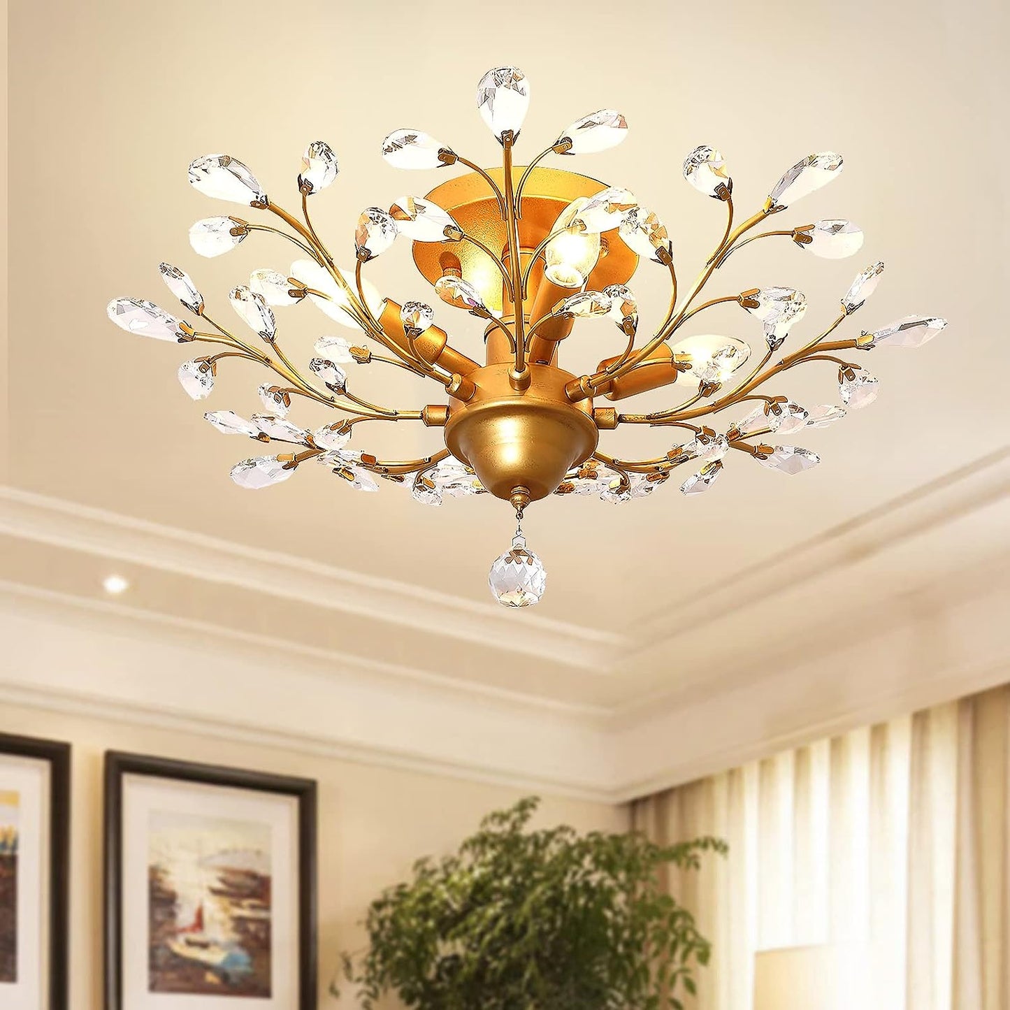 Gold coloured chandelier with crystal accents in a room with framed pictures and a plant.