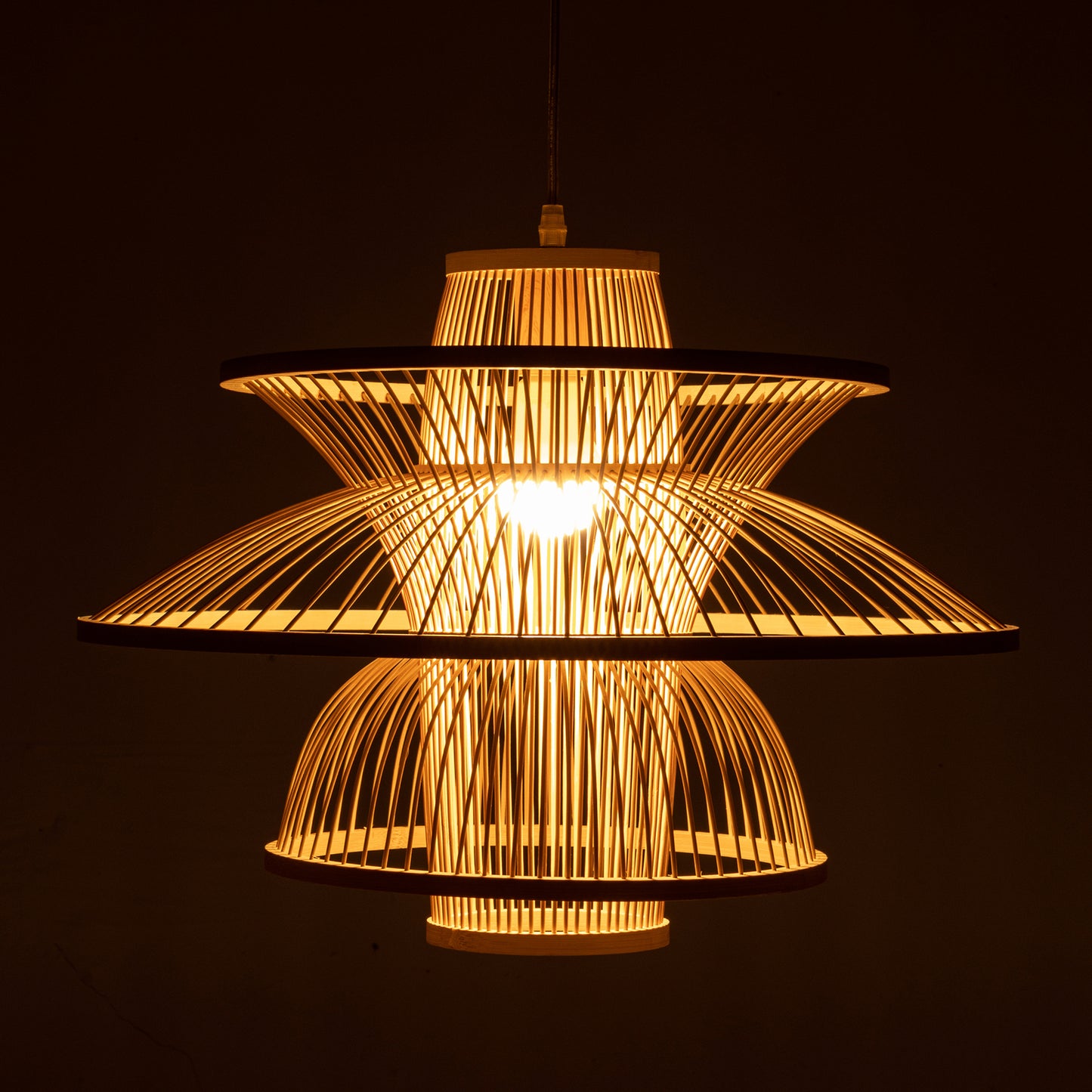 Decorative woven bamboo ceiling light with a three tiered design illuminated against a dark background
