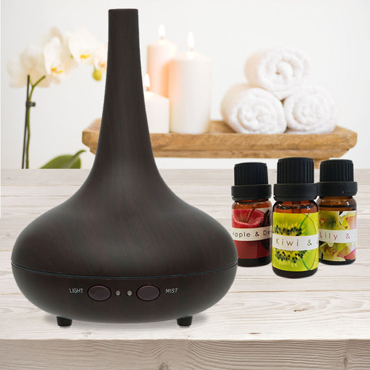Black essential oil diffuser on a wooden surface with bottles of essential oils in the background.