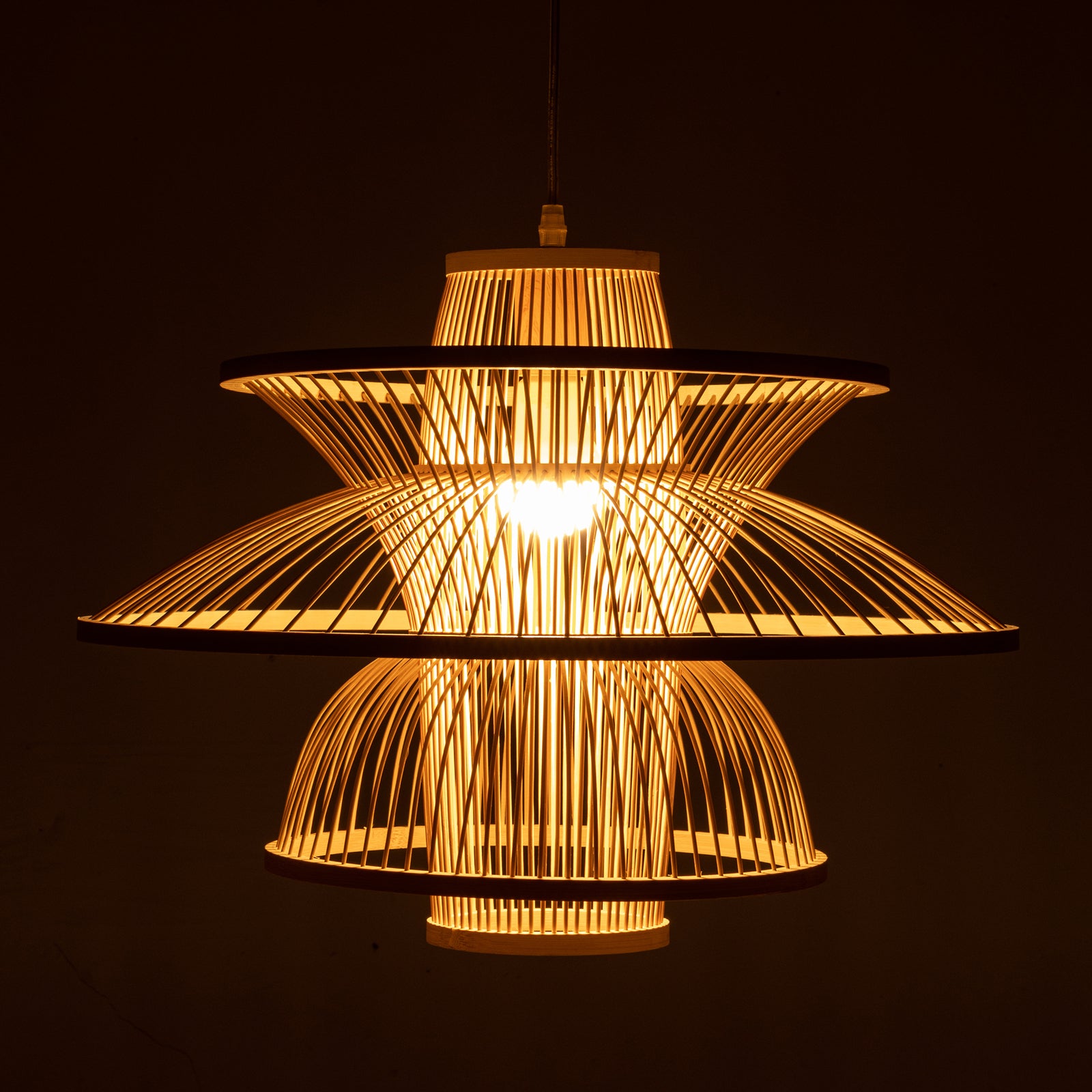 Decorative woven bamboo ceiling light with a three tiered design illuminated against a dark background